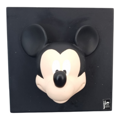 Black square plaque featuring a 3D Mickey Mouse head relief centered on the panel, with a small logo in the bottom-right corner.